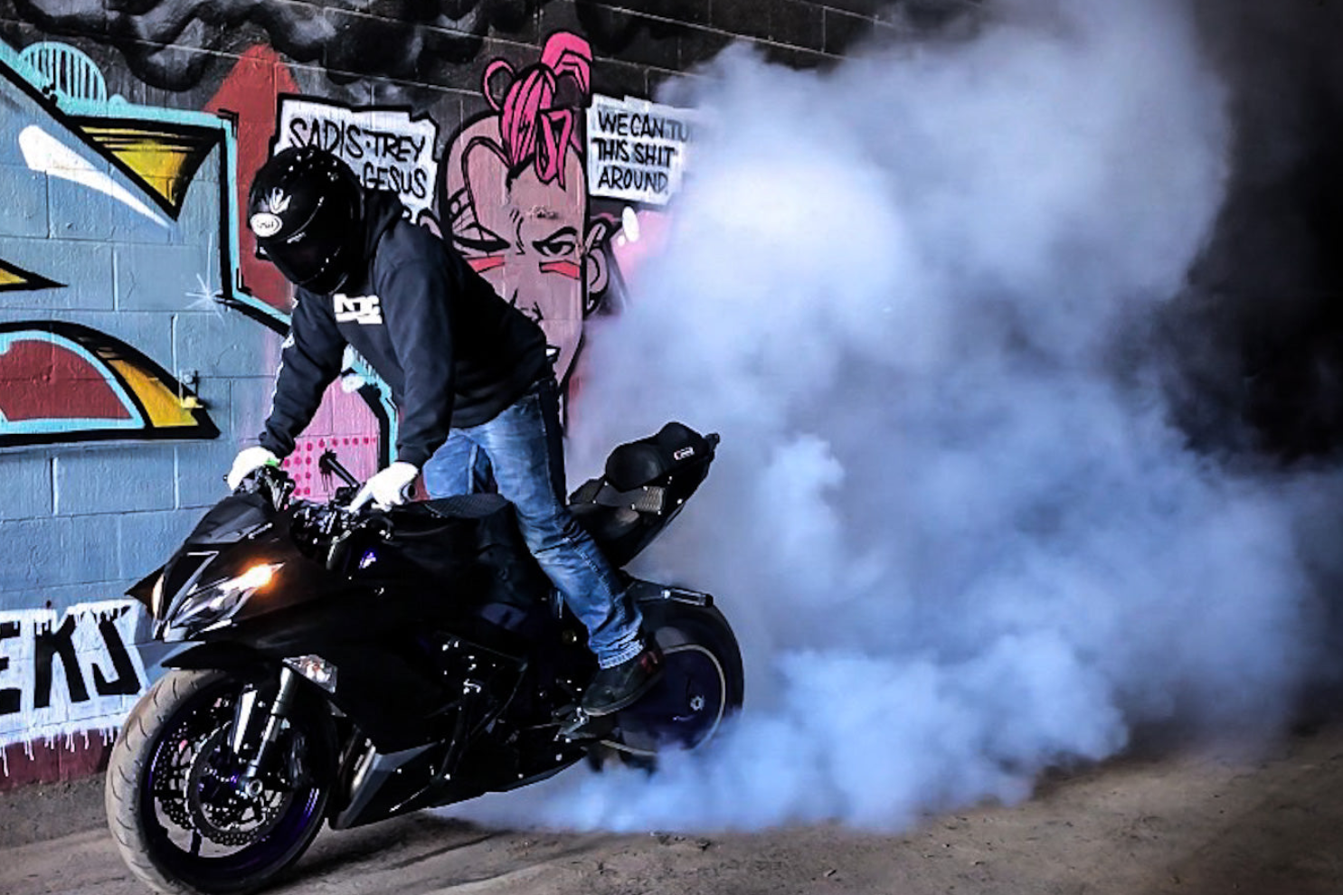 Person on a motorcycle with smoke in front of a graffiti-covered wall